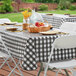 A white folding chair with a black and white checkered tablecloth on a picnic table with a basket of fruit.