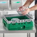 A person putting a glass bowl into a green Cambro dish rack with grey sides.