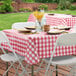 A table set with a burgundy checkered vinyl tablecloth on a table outdoors.