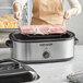 A woman using a Proctor Silex commercial roaster to cook meat.