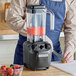 A man in a blue apron blending fruit in a Hamilton Beach commercial blender.