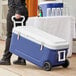 A person pulling a Choice Blue 84 Qt. cooler on wheels using a white tow handle.
