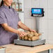 A digital receiving scale with a stainless steel tower and a container of potatoes being weighed on its platform.
