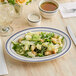 An Acopa ivory stoneware platter with blue bands holding a salad on a table with a glass of liquid.