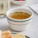 An Acopa ivory stoneware bouillon cup filled with broth on a table with food.