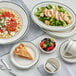 A table with Acopa ivory stoneware bouillon cups with green bands, plates, and bowls of food.