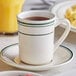 An Acopa ivory stoneware cup with green bands full of tea on a saucer.