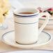 An Acopa ivory stoneware cup with blue bands on a saucer.