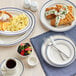 An Acopa ivory stoneware cup with blue bands on a table with plates of food and a cup of coffee.