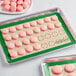 A Baker's Lane green silicone baking mat with pink macarons on a white surface.