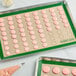 A Baker's Lane green silicone baking mat with pink macarons on it.