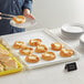 A person holding a white bakery display tray with pastries on it.