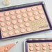 A Baker's Lane purple silicone baking mat with pink and white macarons on it.