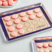 A Baker's Lane purple silicone baking mat with pink macarons on it.