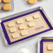 A Baker's Lane purple silicone baking mat with cookies on a table.