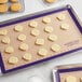 A Baker's Lane purple silicone baking mat on a white baking sheet with cookies.