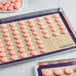 A Baker's Lane purple silicone baking mat with pink macarons on a white surface.