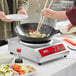 A woman cooking food in a wok on an Avantco countertop induction cooker.