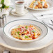 An Acopa stoneware pasta bowl with pasta and basil on a table.