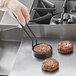 A hand using a Vigor egg ring to cook two meat patties in a pan.