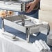 A person holding a metal container on a silver tray with a plate on it.