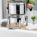 A woman using an Acopa Manchester round chafer stand to hold a large stainless steel pot.