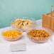 A table with a Cambro pebbled serving/salad bowl of chips, a bowl of goldfish crackers, and a bowl of pretzels.