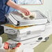 A man preparing a large Acopa stainless steel electric chafing dish on a table.