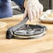 A person using a Choice metal tortilla press to flatten dough.