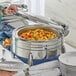 A woman using an Acopa Manchester stainless steel chafer to serve food from a buffet table.