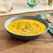 An American Metalcraft matte grey melamine bowl filled with soup and herbs on a table.