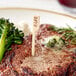 A steak with a Tablecraft bamboo meat marker on a plate with broccoli and cheese.