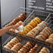 A person's hand reaching into a Choice slant top wire bread basket filled with bagels.