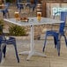 A square silver powder-coated aluminum outdoor dining table with an umbrella hole, surrounded by blue metal chairs.