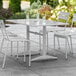 A white Lancaster Table & Seating outdoor dining table with a white umbrella and chairs on an outdoor patio.