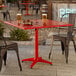 A square red powder-coated aluminum outdoor dining table with an umbrella hole, shown with drinks and food on top.