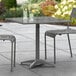 A Lancaster Table & Seating gray metal outdoor table with two chairs on a patio.