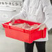 A person in a white coat holding a red container with raw meat.