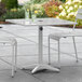 A Lancaster Table & Seating silver outdoor table with chairs and an umbrella pole on a patio.