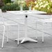 A white table with a black umbrella hole on a patio with two white chairs.