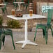 A white powder-coated aluminum outdoor dining table with an umbrella hole, shown with green chairs.