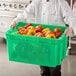 A chef in a white coat holding a green Choice container full of yellow and red bell peppers.