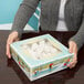 A woman holding a 10" x 10" x 2" white box with a plastic window filled with snowballs.