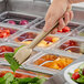 A hand holding a beige plastic salad tong over a salad bar.