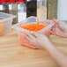 A person holding a Cambro translucent plastic food pan filled with shredded carrots.