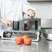 A chef in a white coat and gloves uses a Vollrath straight blade assembly to slice a tomato.