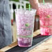A clear 32 oz. compostable plastic cold cup filled with ice and a purple beverage, featuring Greenware branding.