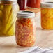 A close-up of a Choice 16 oz. regular mouth glass canning jar with a silver metal lid on a table with other jars of food.