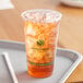 A Fabri-Kal Greenware plastic cup filled with ice and orange liquid on a tray.