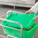 A person in a white lab coat and gloves holding a green Choice meat lug lid.